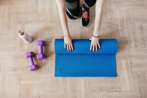 woman unrolling excersize mat on wooden floor with weights next to it