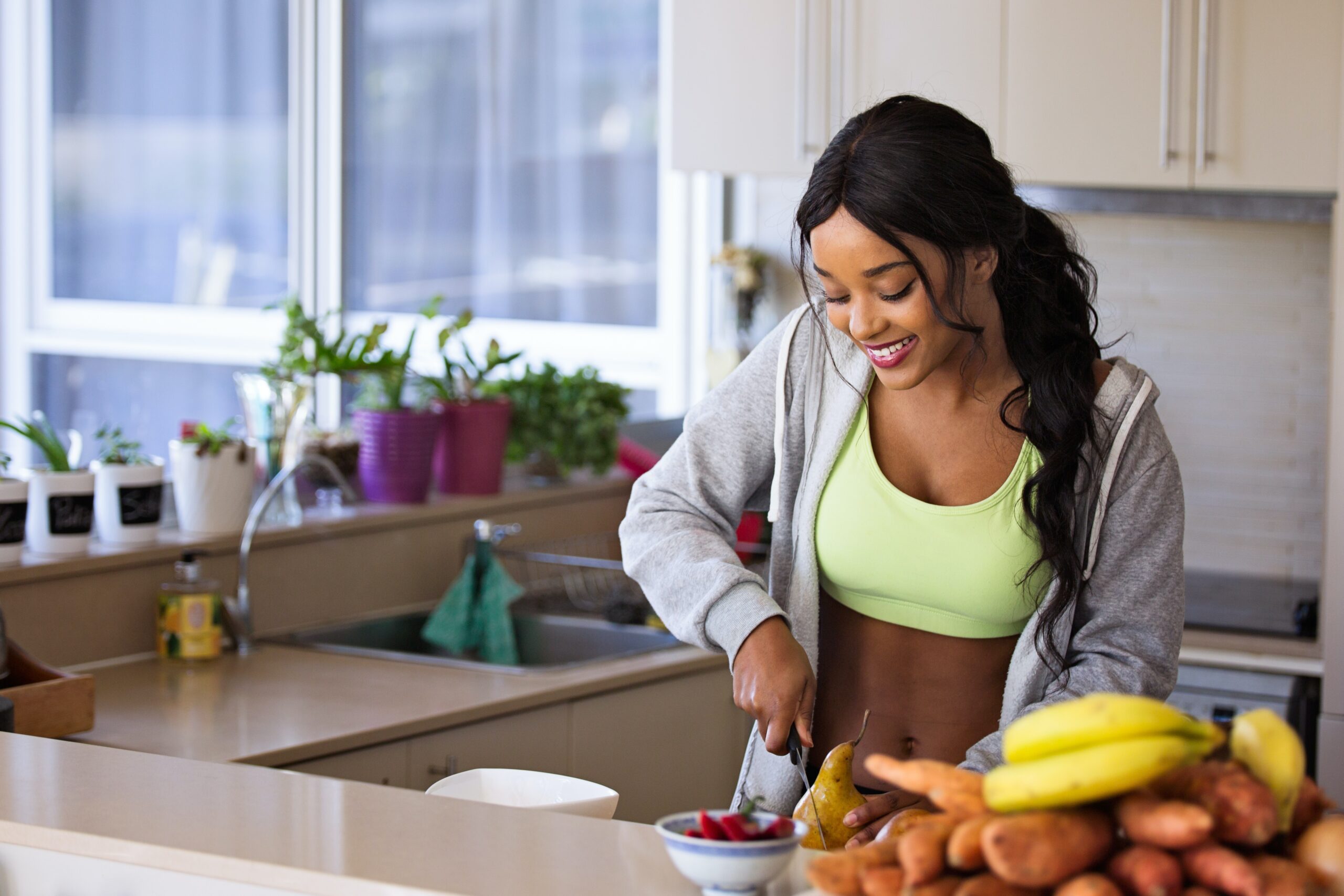 woman wearing athletic clothing chopping a pear in her kitchen next to a bowl of fruit